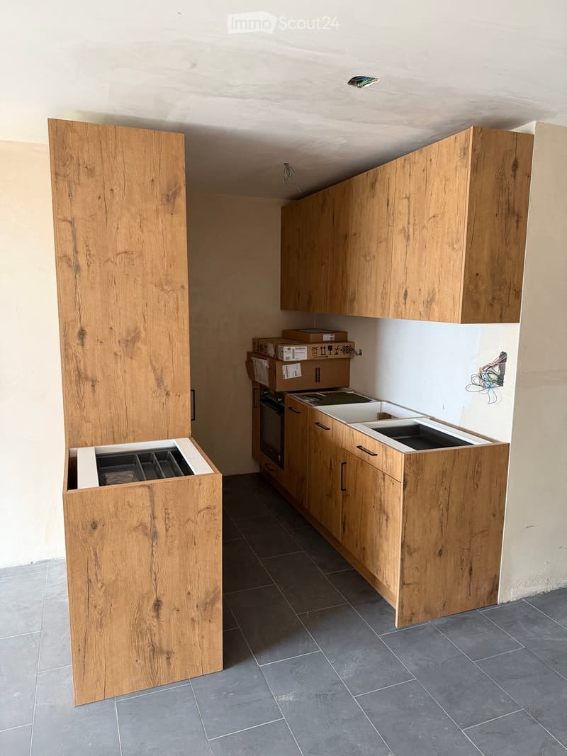 Empty kitchen with wooden cabinets, dark tiled floor, and exposed wiring and boxes on the counter.