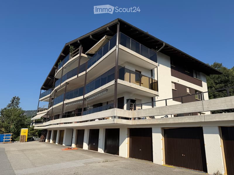 Modern multi-story building with balconies, large windows, and multiple garage doors on the ground floor.