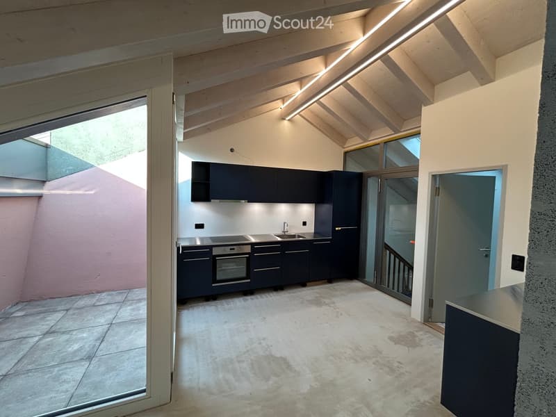 Modern kitchen with dark blue cabinets, stainless steel appliances, and a concrete floor. Features an open layout with large windows and a sliding glass door leading to an outdoor area.