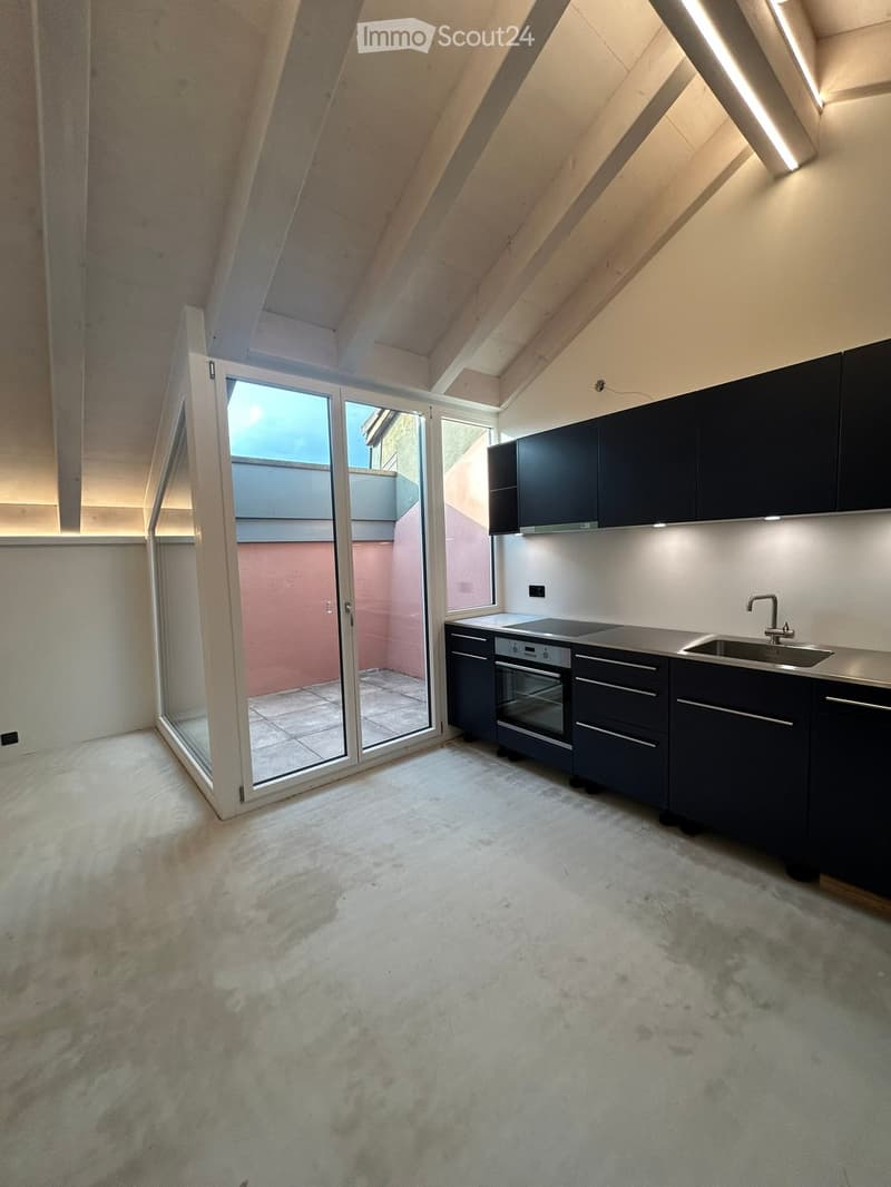 Modern kitchen with dark cabinets, stainless steel oven, sink, and faucet, featuring a large window and sliding glass door leading to a balcony.