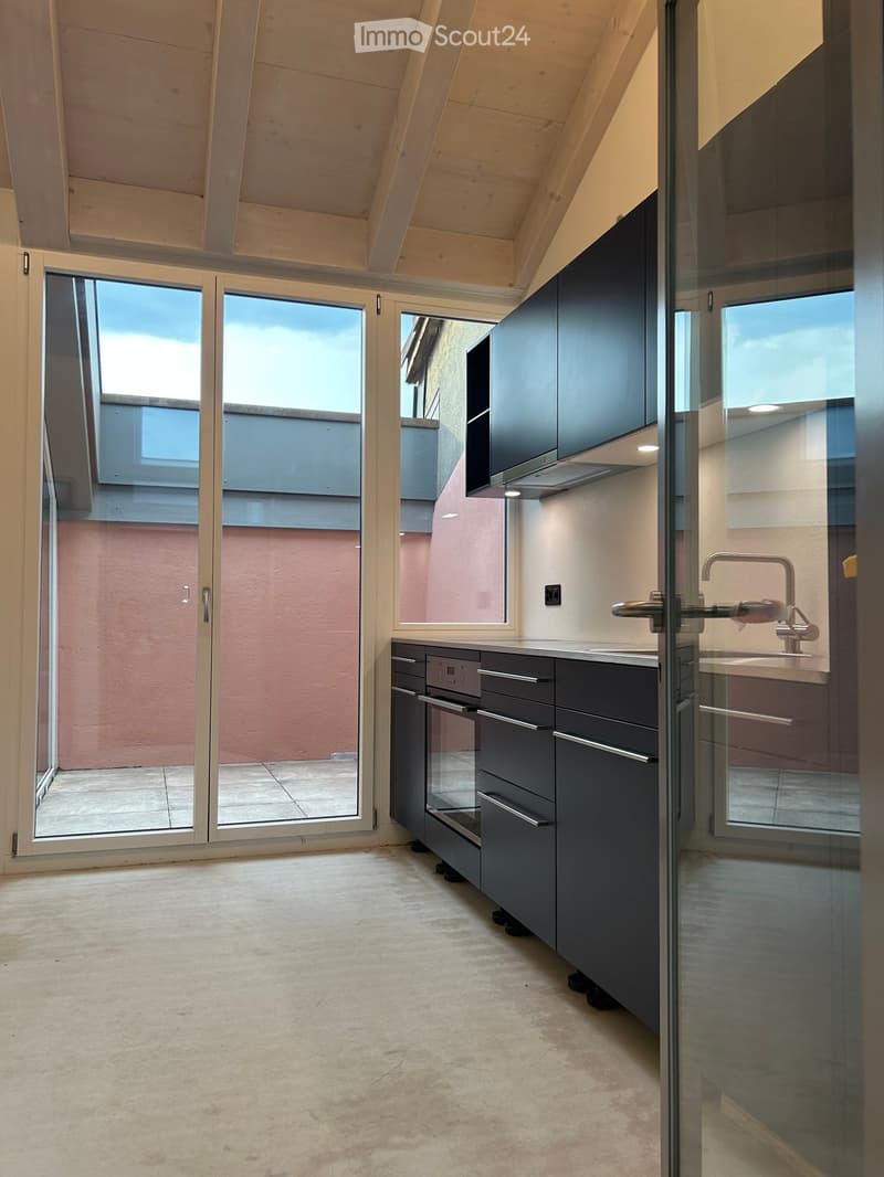 Modern kitchen with dark grey cabinets, a sink, and a faucet, featuring large windows and a glass door leading to an outdoor area.