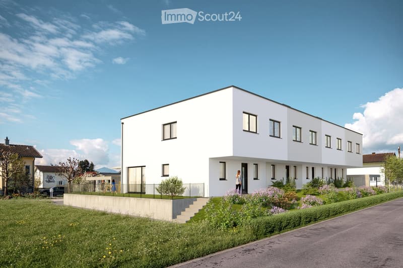 Modern two-story white house with large windows and a flat roof, surrounded by a well-maintained garden and pathway.
