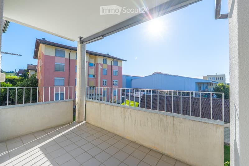 Balcony with tiled floor, metal railing, and retractable awning, overlooking a residential area with buildings and greenery.