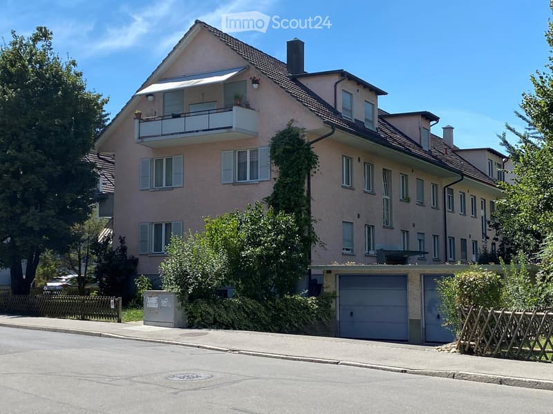 Two-story house with pink facade, multiple windows, balcony on the upper floor, and a garage in the foreground.