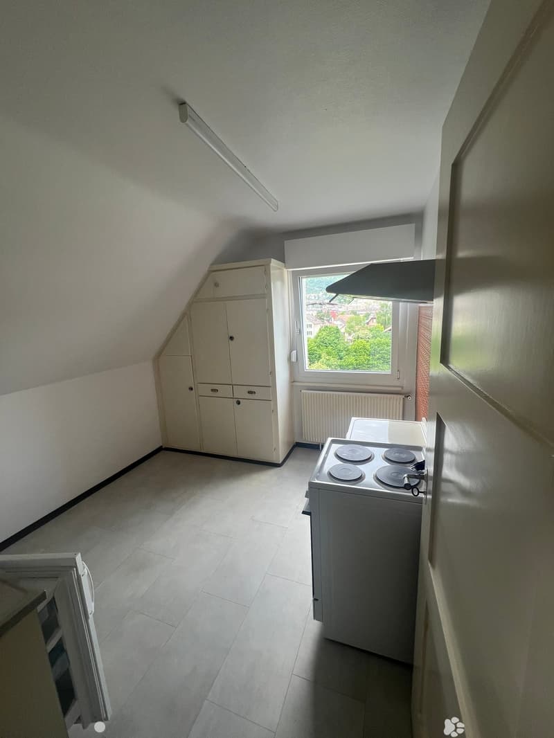Small kitchen with a white tiled floor, a stove with four burners, a cabinet, and a radiator under a window with a view of greenery.