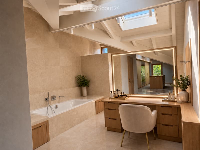 Modern bathroom with a freestanding bathtub, vanity with a large mirror, a plush chair, and decorative items including a vase and candle. The space features warm, textured tiles and ample natural light from a skylight.