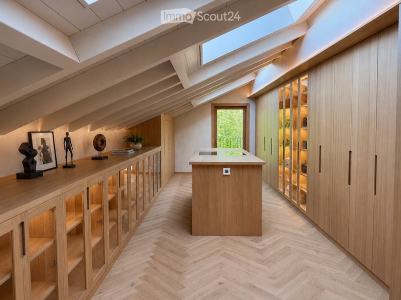 Modern, well-lit room with wooden cabinetry, glass-fronted shelves, a central island, and decorative items on the counter.
