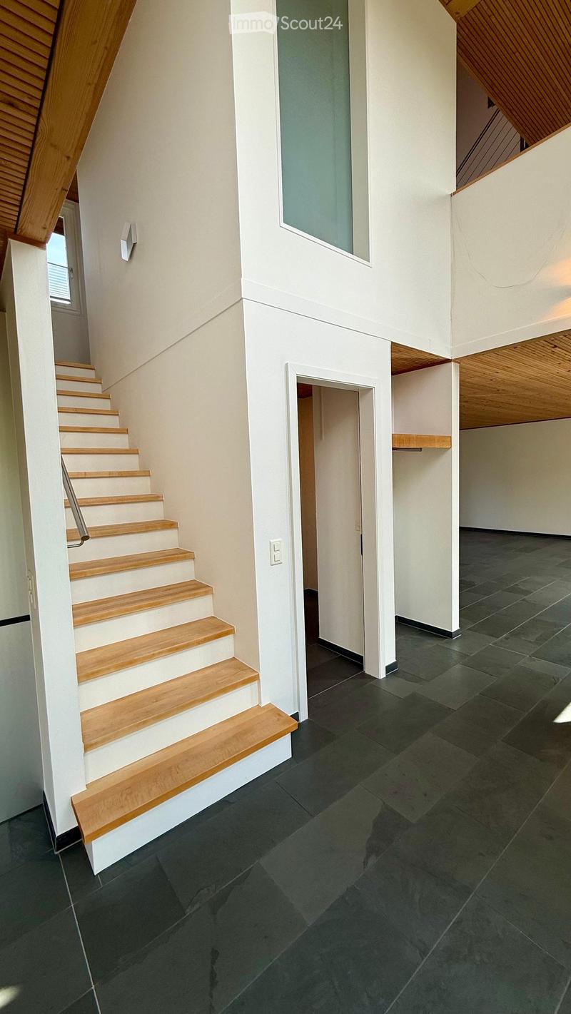 Modern hallway with wooden staircase, dark tiled floor, white walls, and a frosted glass window above the stairs.