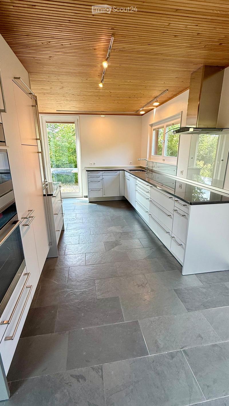 Modern kitchen with white cabinets, stainless steel appliances, dark grey tiled floor, and a large window overlooking a green area.