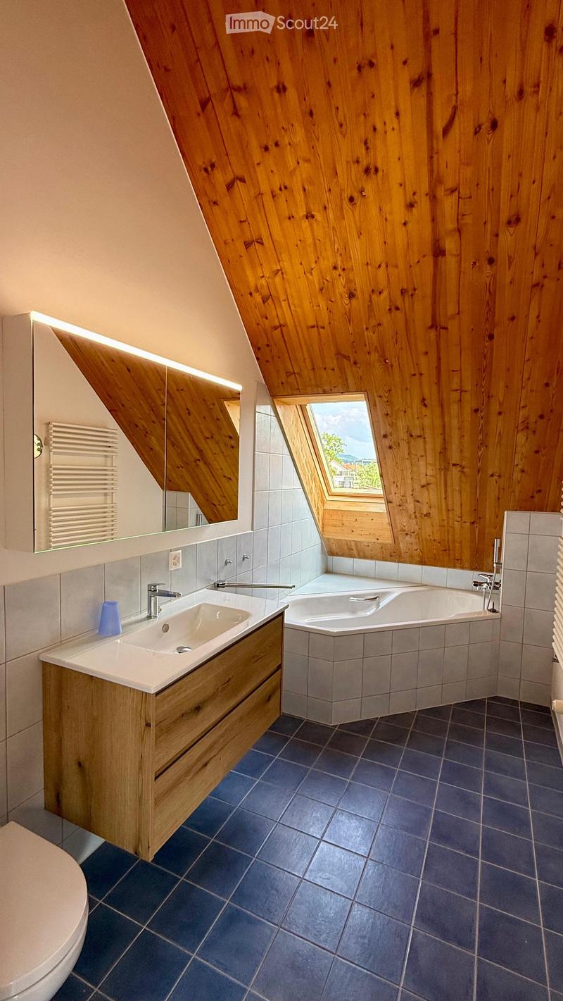 Modern bathroom with wooden walls, skylight window, blue tiles, sink, bathtub, and mirror.