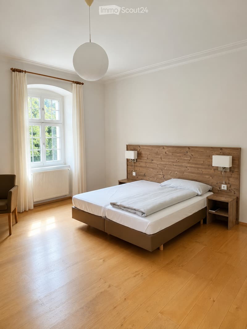 Bright bedroom with wooden flooring, large bed with wooden headboard, nightstands, wall-mounted lamps, and a window with curtains.