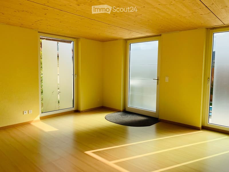 Bright, empty room with yellow walls, wooden floor, and large glass sliding doors leading to an outdoor area.