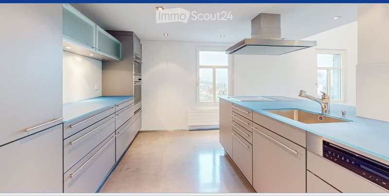 Modern kitchen with light blue countertops, stainless steel appliances, and ample natural light from large windows.