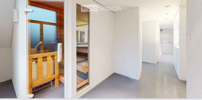 Empty hallway with white walls and a polished concrete floor, featuring a glass door leading to a wooden sauna area.