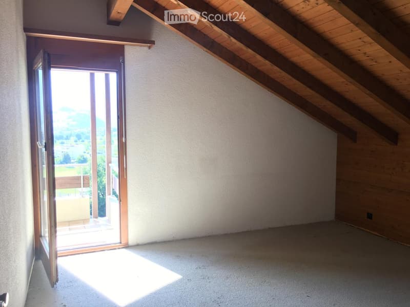 Empty attic room with wooden slanted ceilings, carpeted floor, and an open sliding door leading to a balcony with a scenic view.
