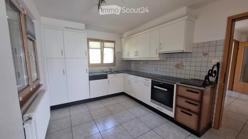 Modern kitchen with white cabinets, tiled backsplash, and stainless steel appliances including an oven and dishwasher. Features a window with blinds and a radiator below.
