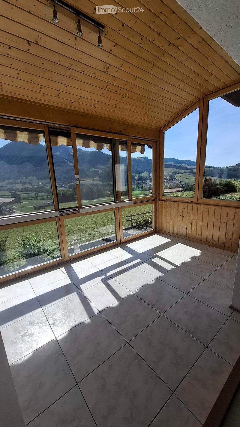 Bright, empty room with wooden ceiling, large windows, and tiled floor, offering scenic mountain views.