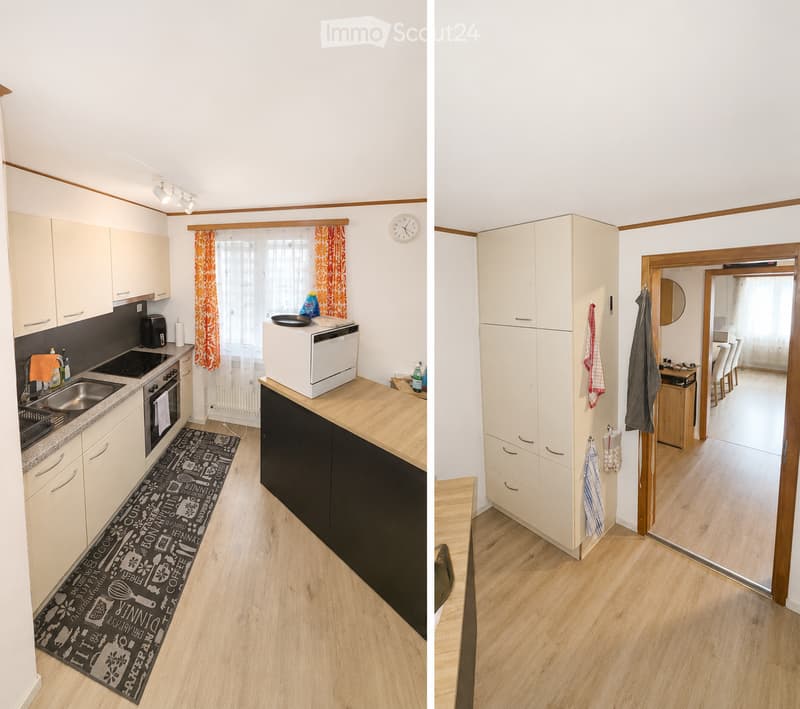 The image shows a modern, well-lit kitchen with light-colored cabinets, an induction stove, a sink, and a microwave on the counter. A kitchen island with a wooden countertop is visible, along with a black rug featuring kitchen-related designs. The adjacen