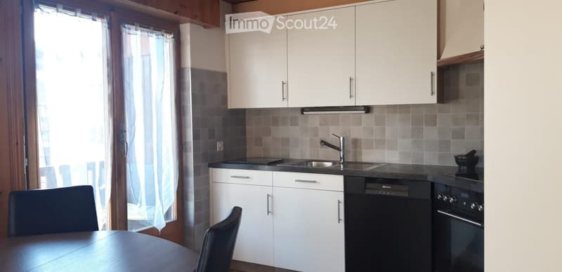 Modern kitchen with white cabinets, black countertops, a sink, dishwasher, oven, and a small dining area with a table and chairs.