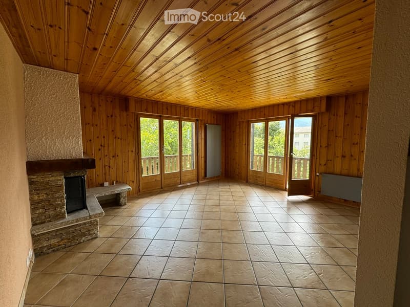 Empty room with wooden walls and ceiling, tiled floor, fireplace, and large windows opening to a balcony.