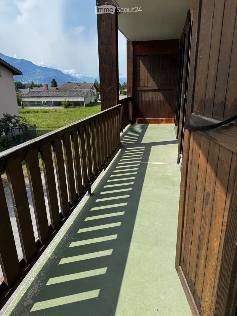 Balcony with wooden railing, green floor, and scenic mountain view in the background.