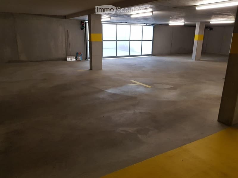 An empty parking lot with concrete floor, metal poles with yellow markings, large glass door, and a broom leaned against the wall