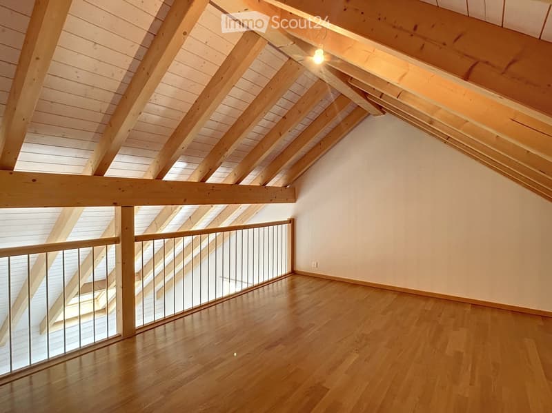 Empty attic space with wooden beams, exposed ceiling, wooden floor, and metal railing leading to another level.