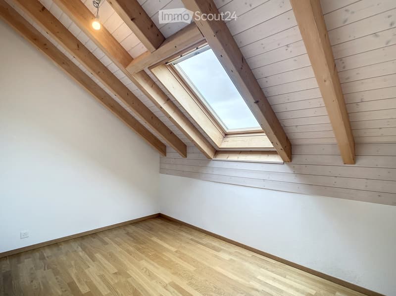 Empty attic room with wooden beams, white walls, wooden floor, and skylight window.