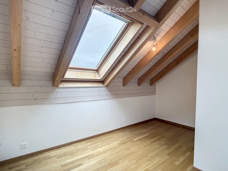 Empty attic room with wooden floor, white walls, exposed wooden beams, and a skylight window.