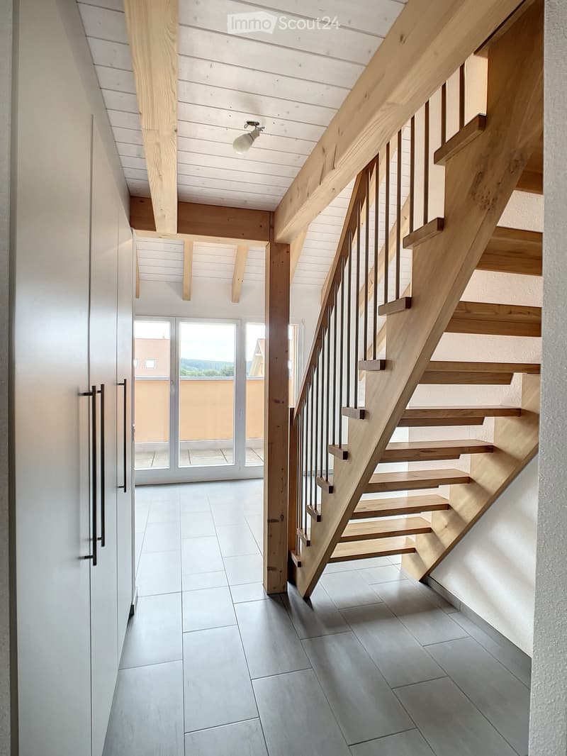 Modern hallway with wooden staircase, white walls, and large glass doors leading to a balcony or outdoor area.