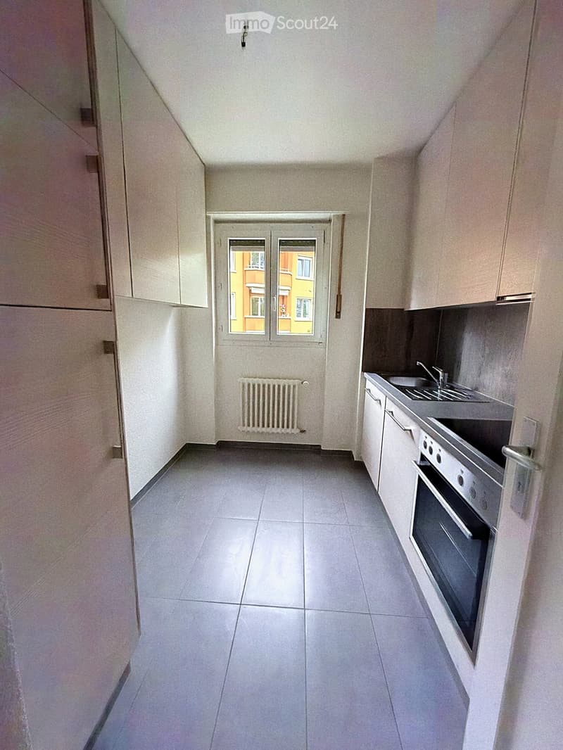 Modern kitchen with tiled floor, white cabinets, stainless steel sink, oven, and radiator under window.