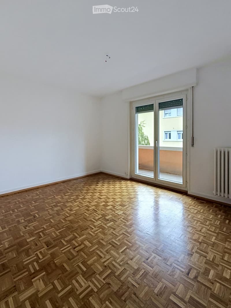 Empty room with wooden herringbone flooring, white walls, and a large sliding glass door leading to a balcony.