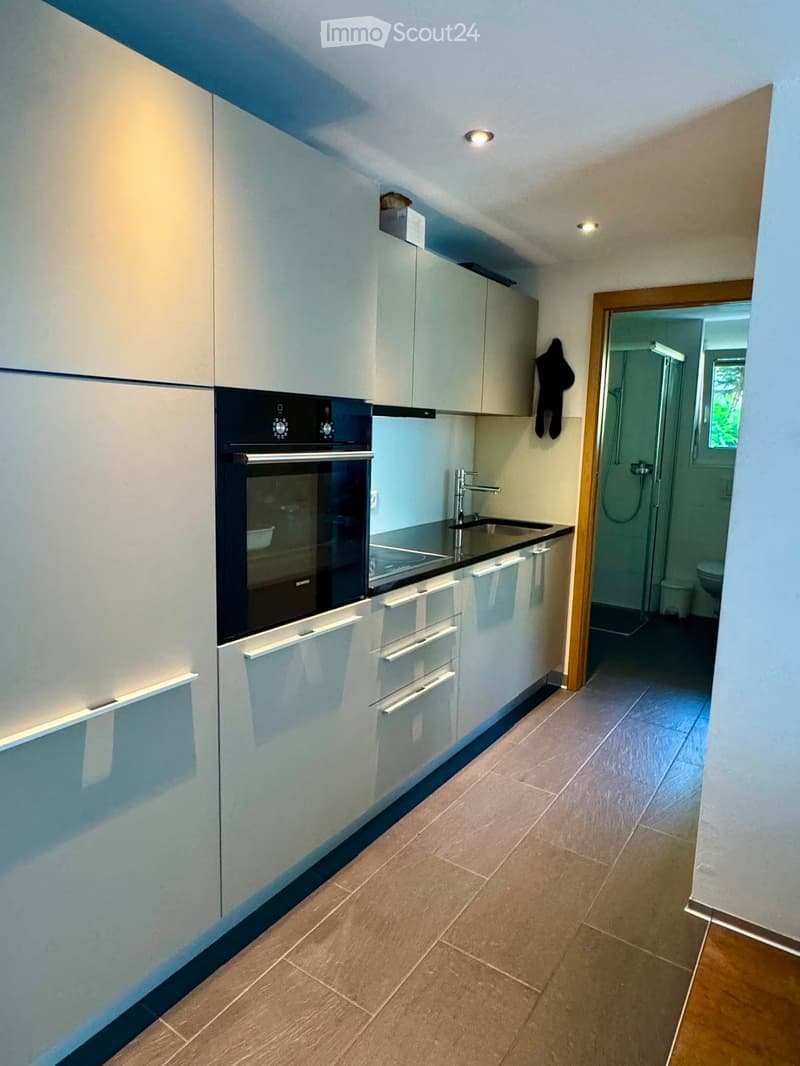 Modern kitchen with white cabinets, a built-in oven, a sink with a modern faucet, and a small adjacent bathroom visible through an open doorway.