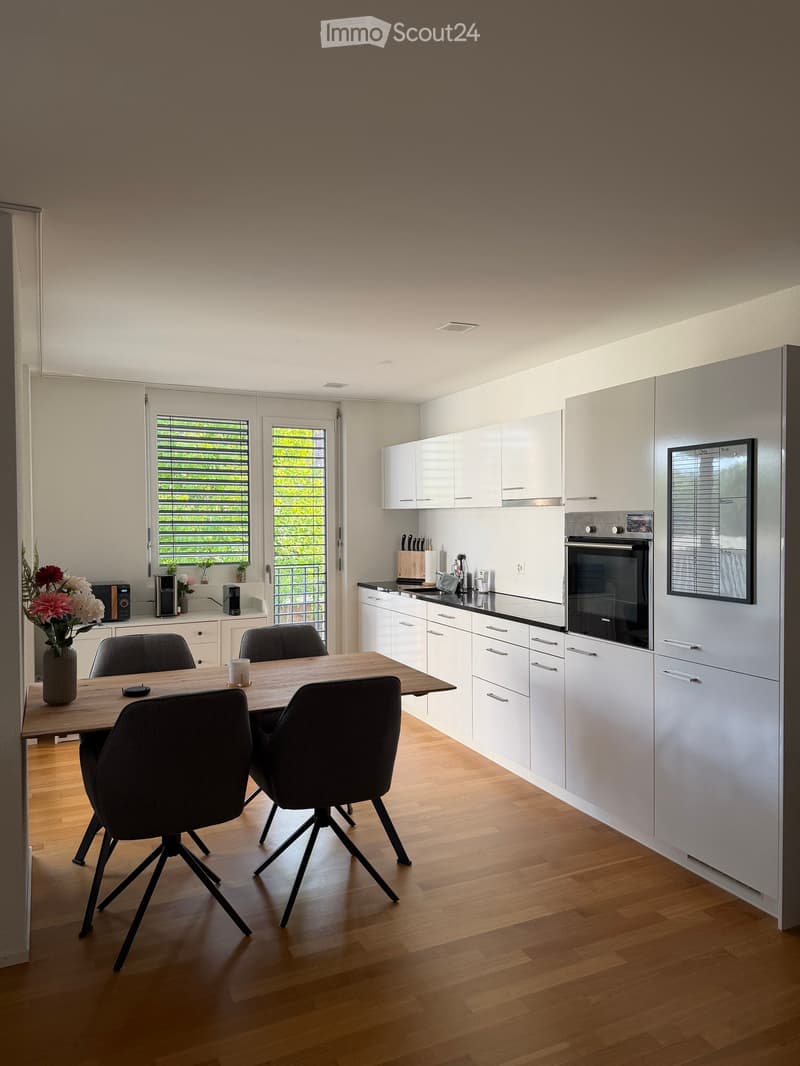 Modern kitchen with white cabinets, wooden floor, dining table with four chairs, and various appliances including an oven and microwave.