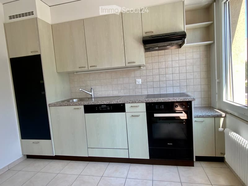 Modern kitchen with light-colored cabinets, granite countertop, stainless steel sink and faucet, built-in oven, dishwasher, and radiator.