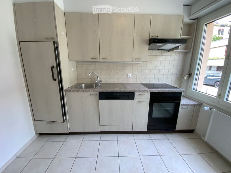 Modern kitchen with light wood cabinets, stainless steel appliances, granite countertop, and tiled floor.