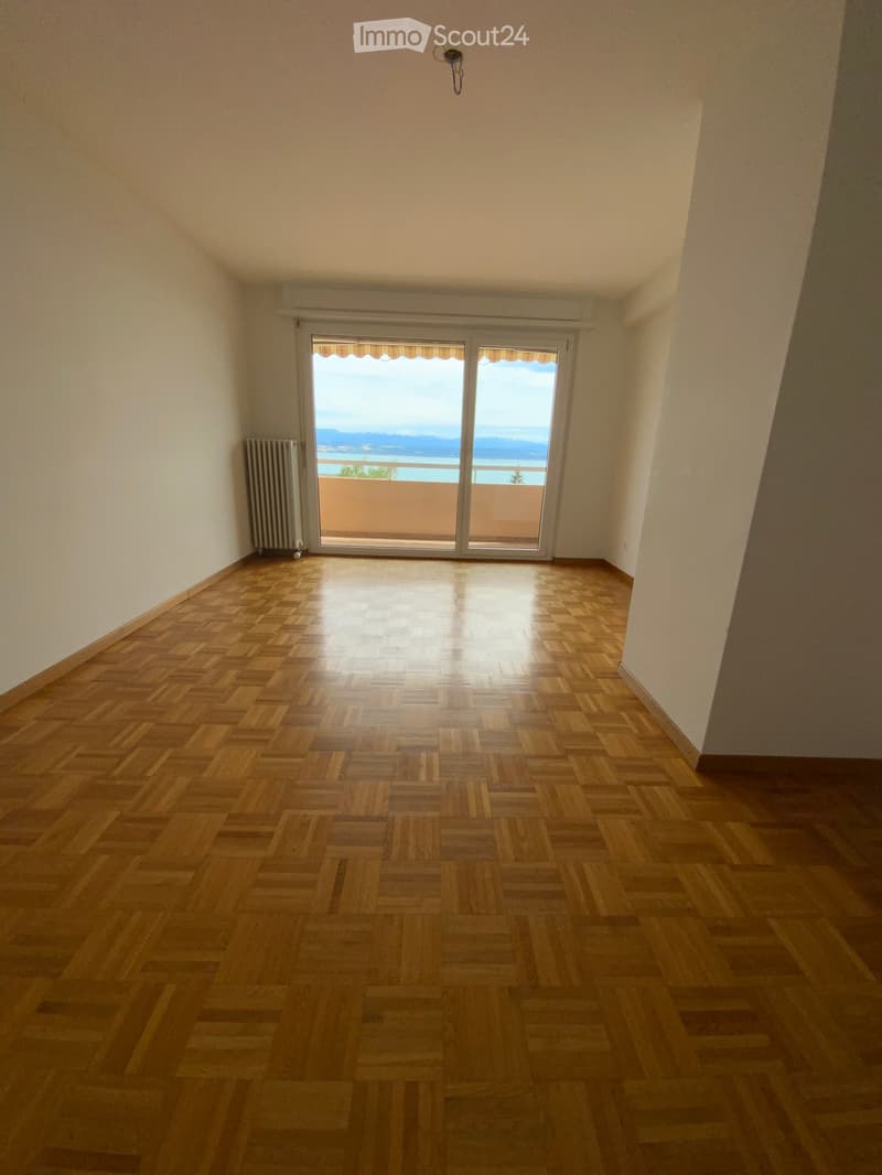 Empty room with wooden parquet flooring, white walls, and large sliding glass doors leading to a balcony with a scenic view.