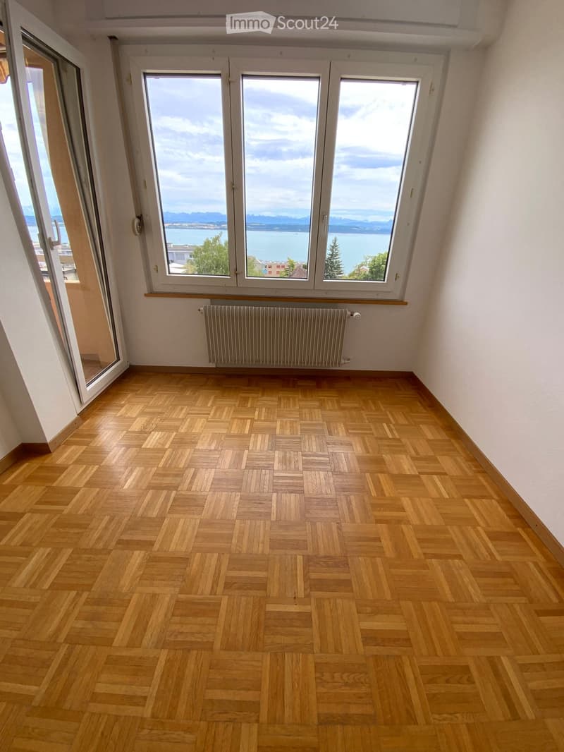 Empty room with wooden parquet flooring, large windows offering a scenic view, and a radiator below the windows.