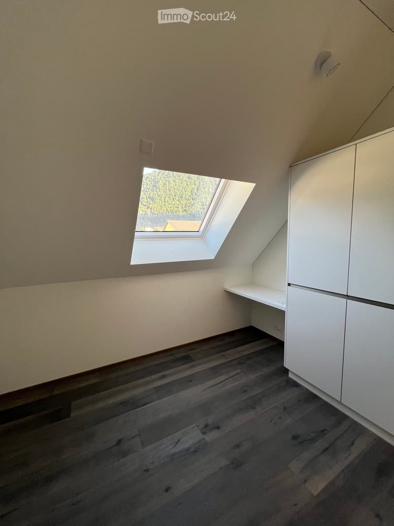Empty room with wooden flooring, white cabinetry, and a skylight window offering a view of trees and a house outside.