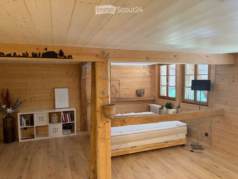 Cozy wooden bedroom with a large bed, wooden shelves, a hanging basket, and a floor lamp near the windows.