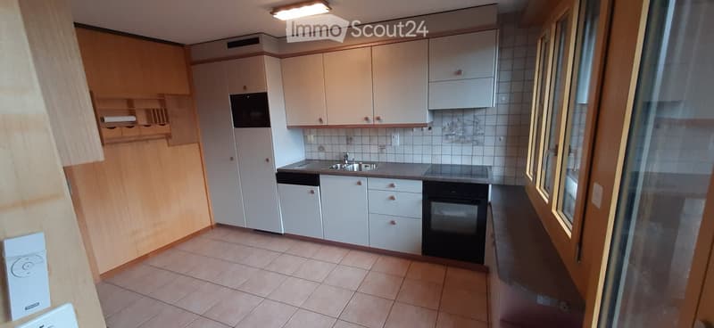 Modern kitchen with white cabinets, stainless steel sink, oven, and dishwasher. The space features tiled flooring and a large window providing natural light.