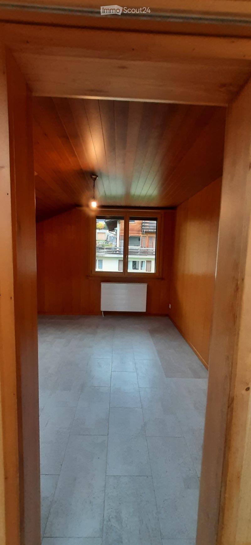 Empty hallway with wooden walls, tiled floor, and a radiator. A window at the end provides natural light.