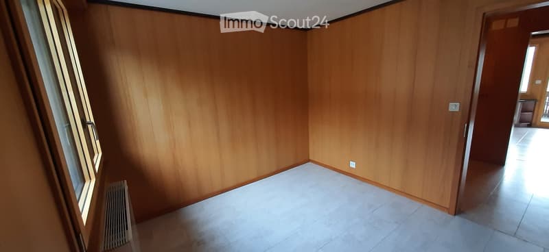 Empty room with wooden walls, tiled floor, and large window with radiator below. No furniture or equipment present.
