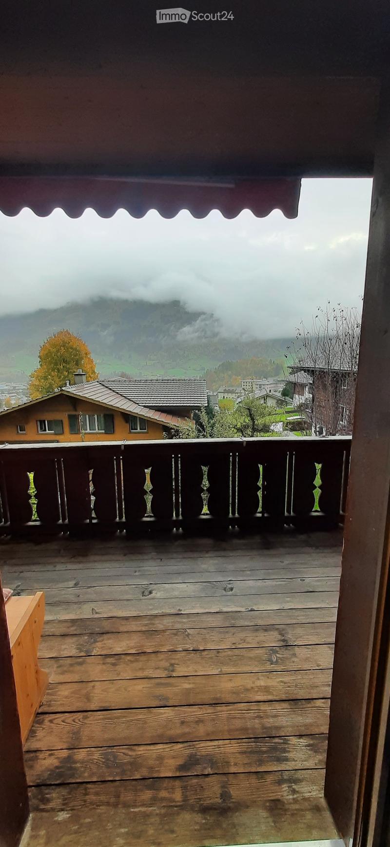 Wooden balcony with railing overlooking a scenic mountain view and town.
