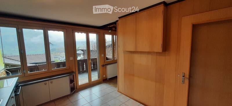 Empty room with wooden cabinets, large windows, and a sliding glass door leading to a balcony with a scenic view.