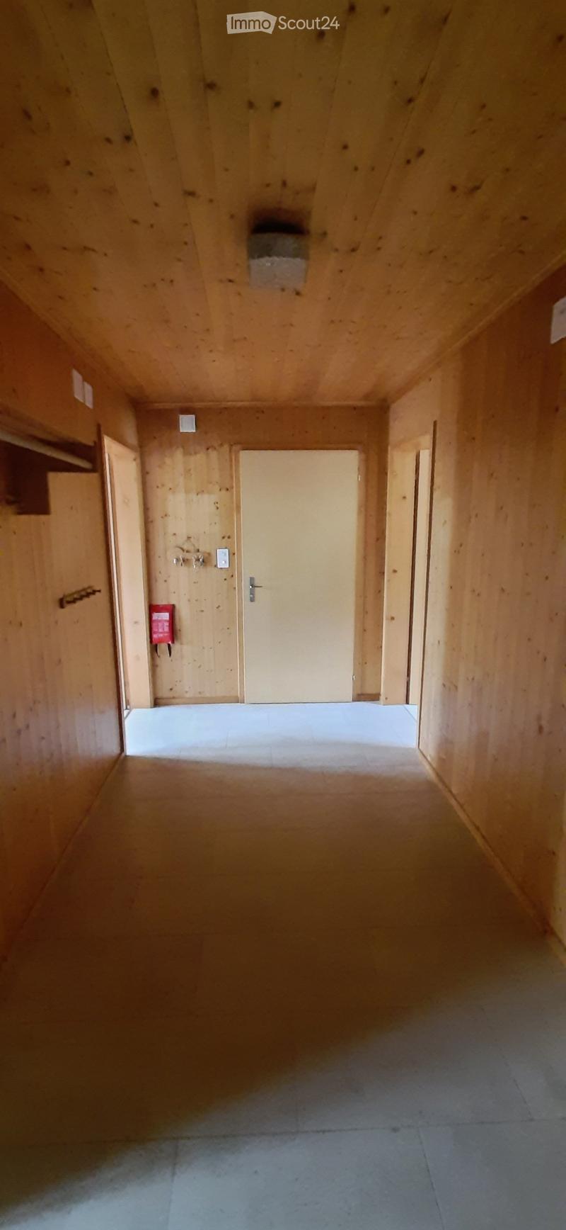 Empty wooden hallway with tiled floor, multiple doors, and a fire extinguisher mounted on the wall.