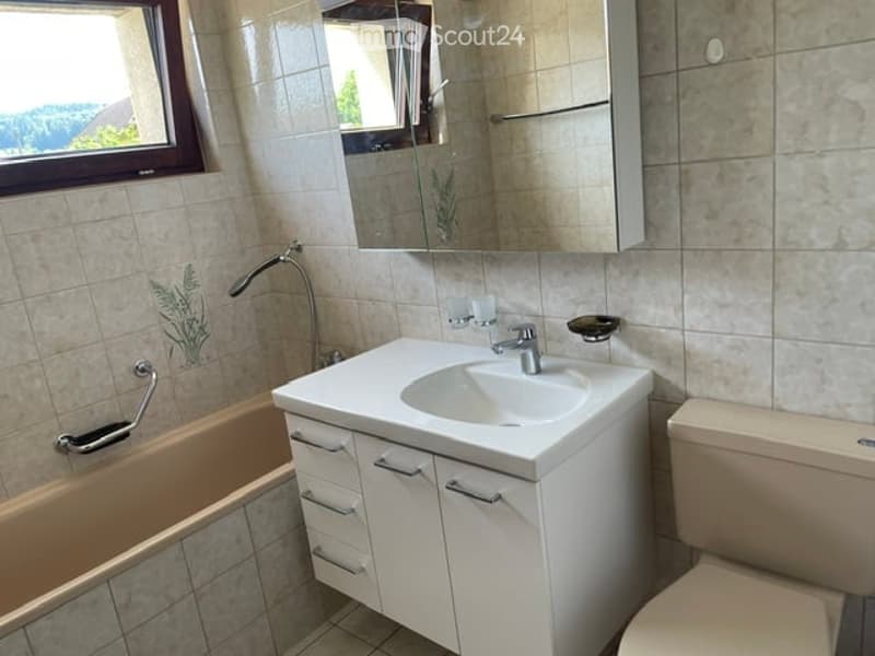Modern bathroom with a white sink, mirror, toilet, bathtub, and cabinet. The walls are tiled with a decorative plant design, and there is a window providing natural light.