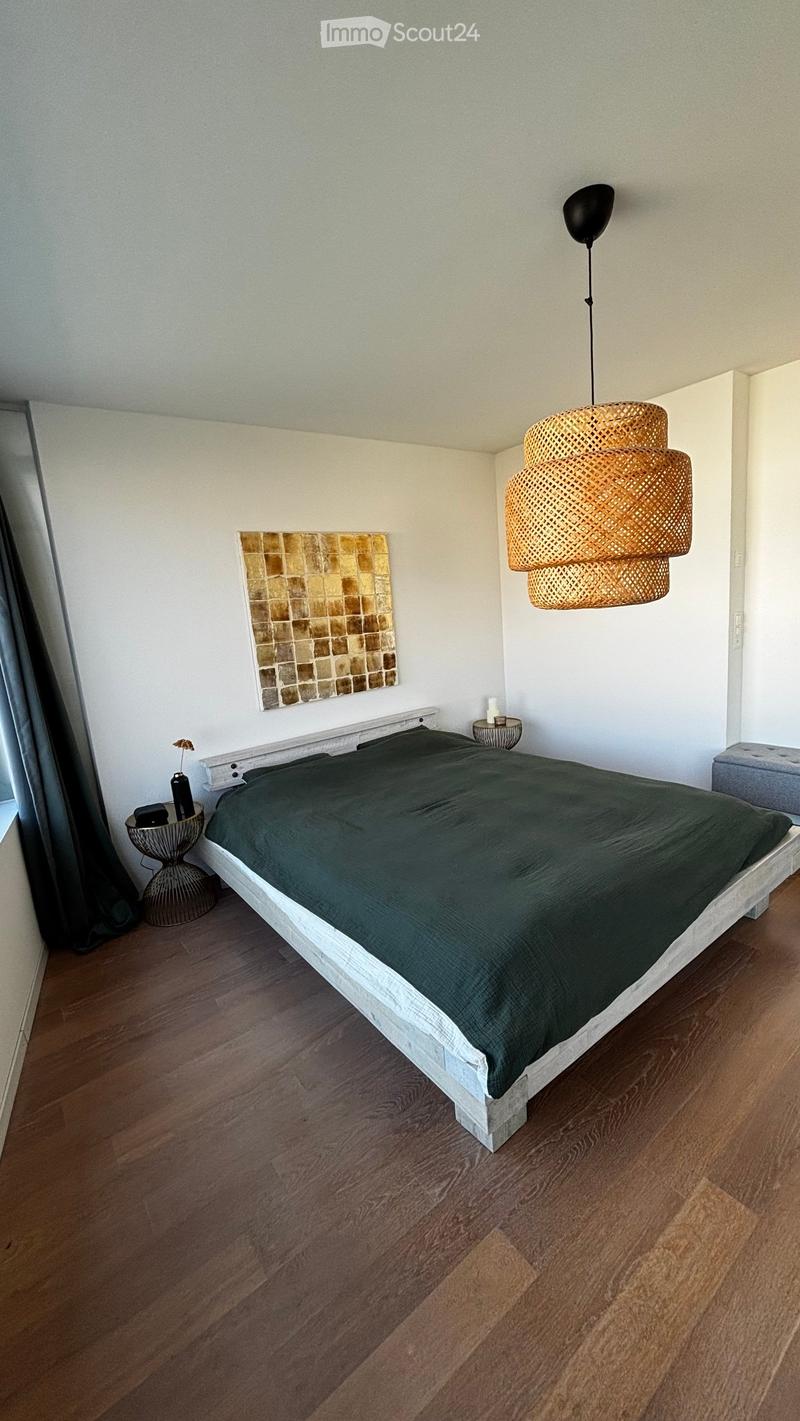 Modern bedroom with a wooden bed, dark green duvet, nightstands, a hanging woven lamp, and a decorative picture frame on the wall.