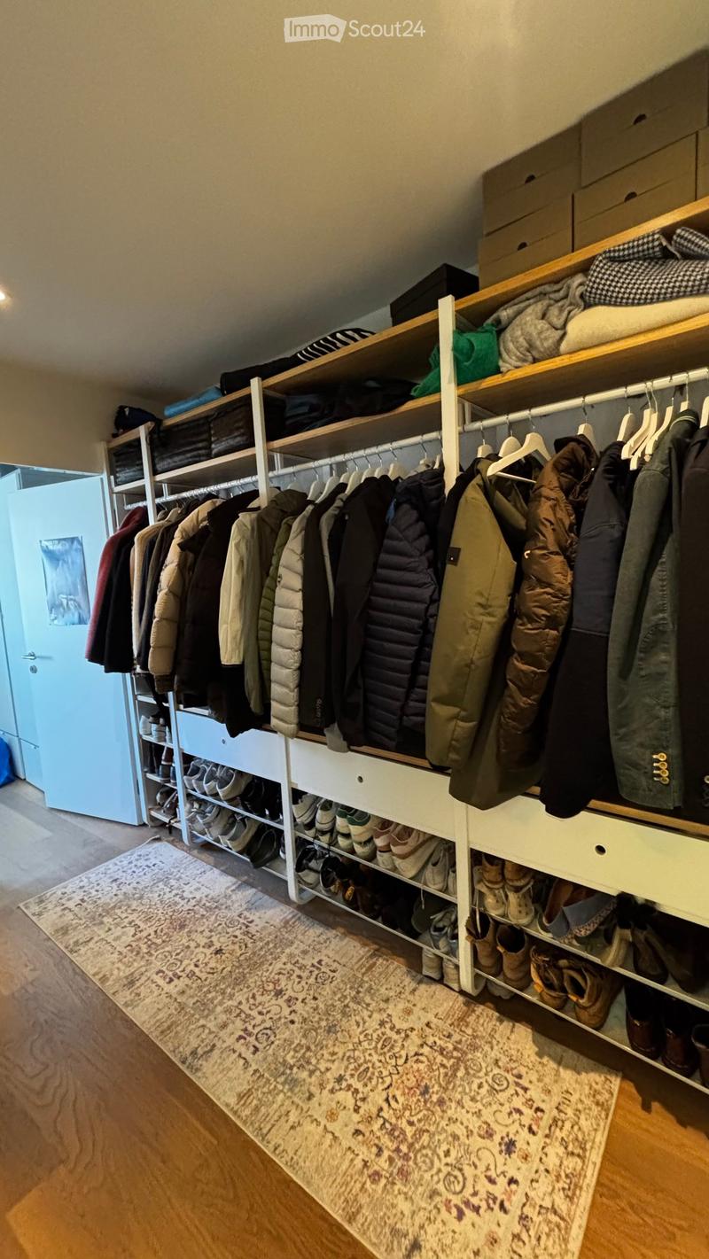 Well-organized walk-in closet with wooden shelves, hanging clothes, and neatly arranged shoes on lower shelves.