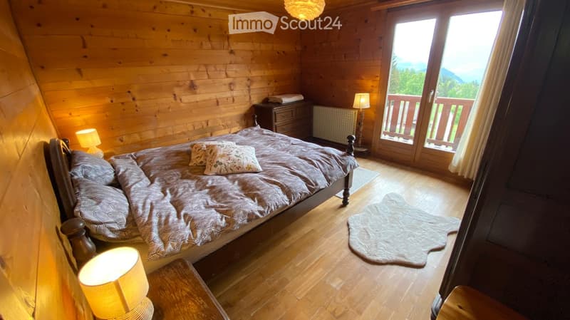 Cozy wooden bedroom with a large bed, nightstands, lamps, and a scenic mountain view through large windows.